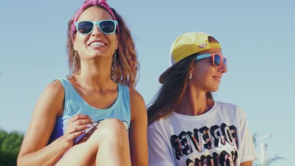 Hübsche Frauen mit Brille sitzen am Strand am Meer, reden, lachen und lächeln. — Stockvideo