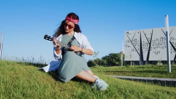 Vrouw die ukelele gitaar speelt in modern park — Stockvideo