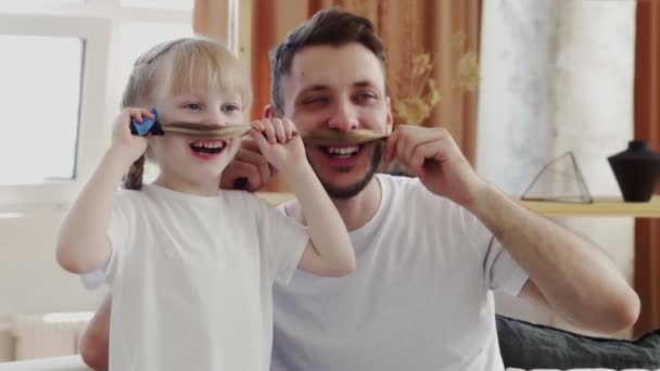 Lustiger Vater und seine Tochter machen Schnurrbart und posieren. Vatertagskonzept — Stockvideo