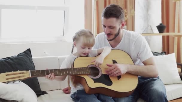 Giovane padre insegna figlia a suonare la chitarra a casa — Video Stock