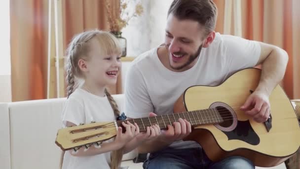 Молодий батько вчить дочку грати на гітарі вдома — стокове відео