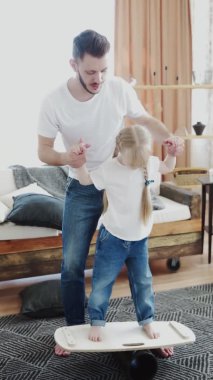 Genç babanın dikey videosu kızına denge tahtasının üzerinde durmasını öğretiyor.