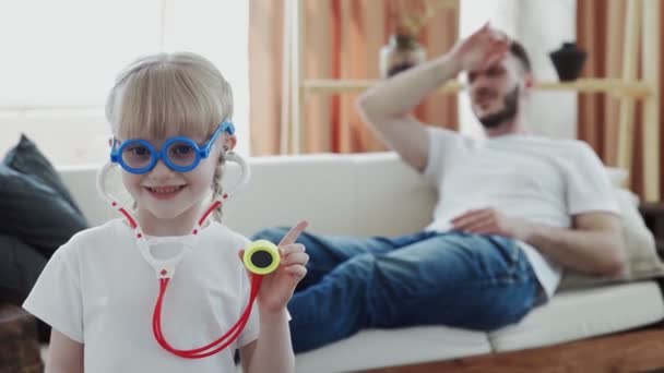 Little funny kid girl dressed in medical uniform playing as doctor with father at home — Stock Video