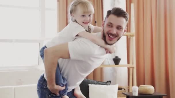 Szczęśliwa rodzina kochający tata daje słodkie małe śmieszne dziecko córka piggyback jazdy przędzenia w domu. Koncepcja dnia ojców — Wideo stockowe