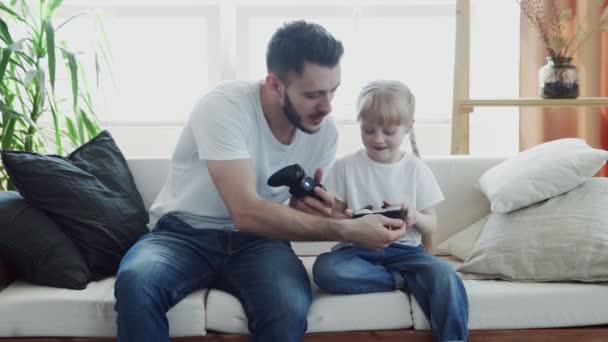 Радісний тато і маленька дівчинка грають у відеоігри з елементами керування в руках вдома . — стокове відео