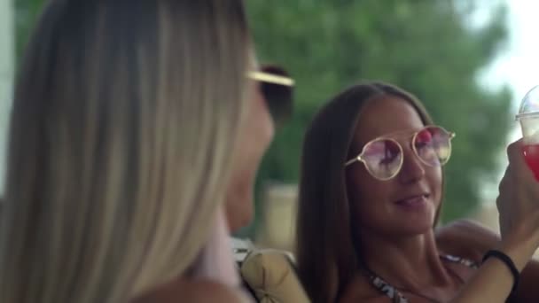 Glada kvinnor i solglasögon njuter av en drink på vackra stranden — Stockvideo