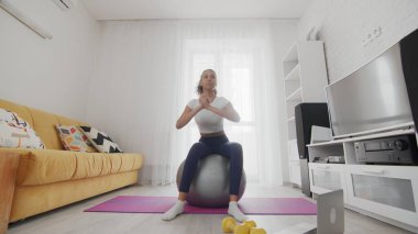 Evde çalışan bir kadın, evdeki dizüstü bilgisayarında eğitmeninin yardımıyla internet hizmetlerini kullanıyor. Zayıf sporcu Afrikalı Amerikalı kadın fitball üzerinde rotasyon egzersizi yapıyor.