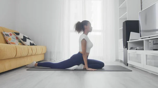 Slim sporty african american woman practicing yoga on a mat. Young woman doing yoga workout in room Royalty Free Stock Photos