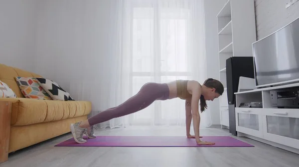 Retrato de una hermosa mujer deportiva delgada practicando yoga en una esterilla. Mujer en ropa deportiva realizar ejercicio de posición de tablón en la estera —  Fotos de Stock