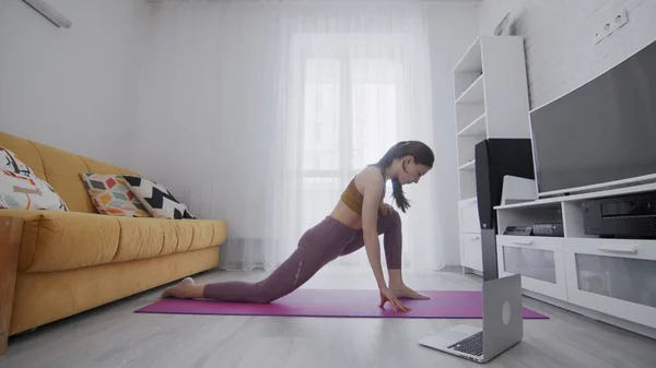 On-line work out woman using internet services with help of her instructor. Portrait of a beautiful slim sporty woman practicing yoga on a mat. Woman doing stretching exercises on violet mat