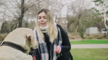 Genç kadın parkta Labrador Retriever köpeğiyle oynuyor.