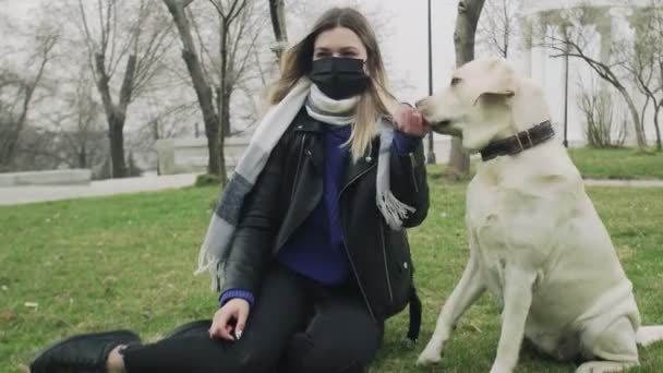 Woman sits on ground and plays with her labrador dog in the park during the quarantine coronavirus COVID-19 pandemic — Stock Video