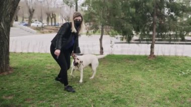 Siyah maskeli çekici bir kadın 2019-2020 Coronavirus karantinası sırasında labrador köpeğiyle parkta oynuyor.