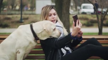 Labrador köpeği olan genç bir kadın parkta bankta selfie çekiyor..