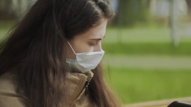Молода жінка в захисній масці використовує смартфон для голосового повідомлення в міському парку. Пандемія Covid-19 захист від коронавірусу . — стокове відео