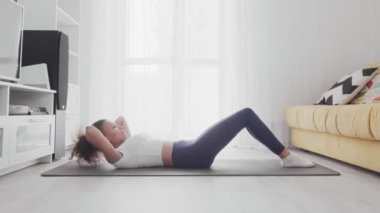 Genç Afro-Amerikan kadın evde yoga minderiyle karın kasları egzersizi yapıyor..
