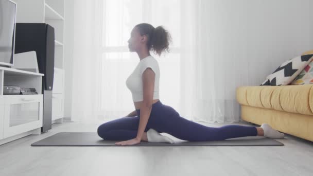 Junge sportliche Afroamerikanerin praktiziert Yoga zu Hause. Frau macht Übungen auf Matte im hellen Raum — Stockvideo