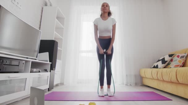 Ung, sportslig, amerikansk kvinne som trener med motstandsbånd på matta med hjelp av instruktøren på PC hjemme – stockvideo