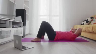 Evde dizüstü bilgisayarında eğitmeninin yardımıyla karın kası egzersizi yapan genç bir transseksüel homoseksüel.