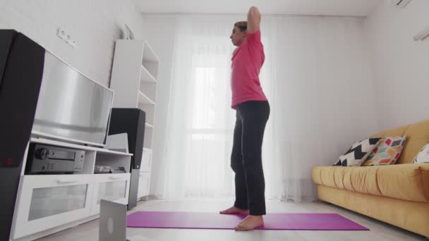 Young transgender homosexual man with makeup does squats on fintes mat at home — Stock Video