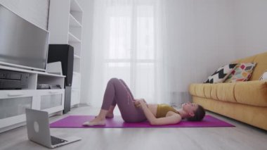 Genç ve güzel bir kadın köprü pozisyonunda duruyor ve dambılı kaldırıyor.