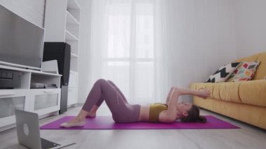 Dövmeli genç bir kadın minder üzerinde karın kasları egzersizi yapıyor.