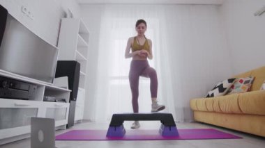 Genç ve güzel bir kadın bir platforma atlıyor ve online talimatlarla dizüstü bilgisayara bakıyor.