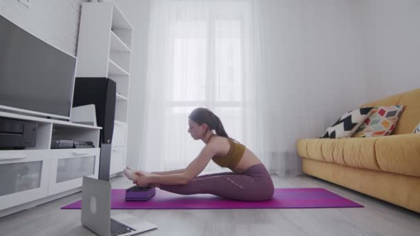 Joven hermosa mujer está haciendo ejercicios de estiramiento en estera violeta en casa — Vídeos de Stock