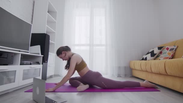 Молодая красивая женщина делает растяжку ног упражнения на фиолетовый мат дома — стоковое видео