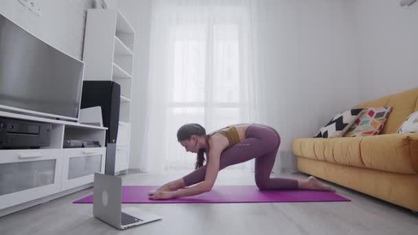 Молодая красивая женщина делает упражнения на растяжку фиолетовый мат дома — стоковое видео