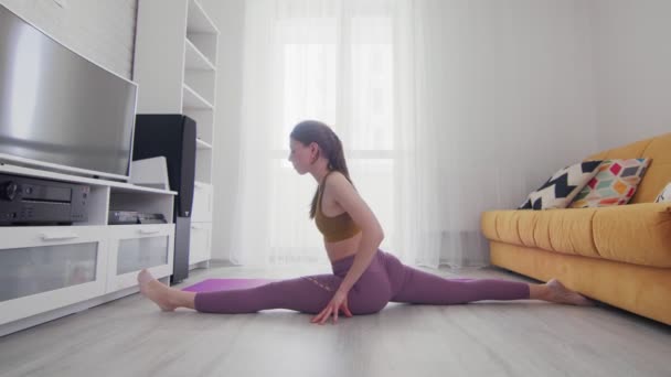 Jonge mooie vrouw doet splits oefening op violette mat thuis — Stockvideo