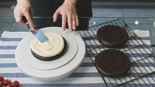 Profi-Koch kocht Kuchen. Junge attraktive Hausfrau bringt mit Metallspachtel weiße Sahne auf Schokoladenkuchen — Stockvideo