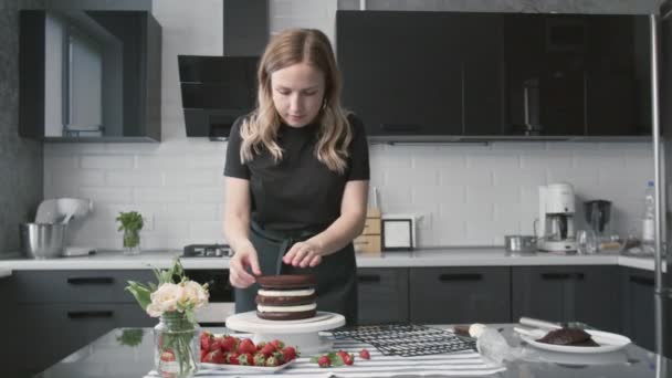 Profi-Koch kocht Kuchen. Junge attraktive Hausfrau macht süßen Schokoladenkuchen mit weißer Sahne und Erdbeere — Stockvideo