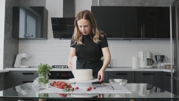 Professionell kock lagar tårta. Ung attraktiv hemmafru använder metall spatel justerar vit grädde på chokladkaka — Stockvideo