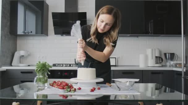 El chef profesional está cocinando pastel. Joven ama de casa atractiva pone crema blanca en la parte superior de pastel de chocolate — Vídeo de stock