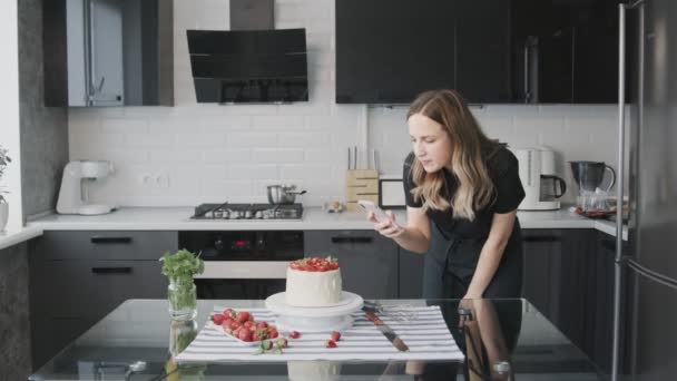 Confectionery blog. Woman in black shirt photographing cake decorated with strawberry. — Stock Video