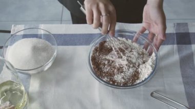 Profesyonel şef kek pişiriyor. Genç ve çekici ev hanımı un ve kakaoyu karıştırmak için metal çırpıcı kullanıyor.