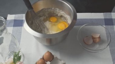 Profesyonel şef kek pişiriyor. Genç çekici ev hanımı karışık yağ ve şekere yumurta ekler.