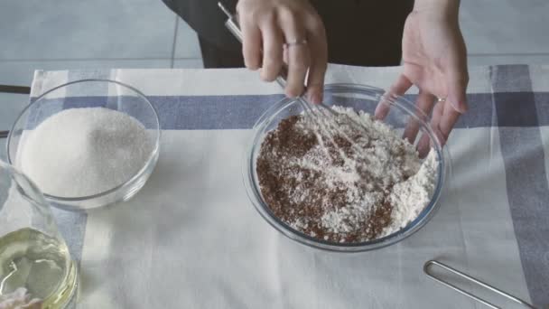 Chef profissional está cozinhando bolo. Jovem dona de casa atraente usa batedor de metal para misturar farinha e cacau na tigela — Vídeo de Stock
