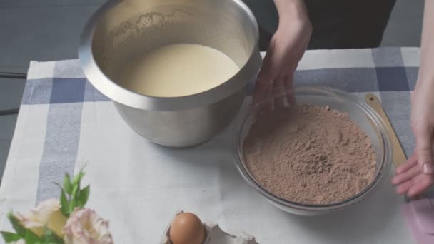 El chef profesional está cocinando pastel. Vista superior de ama de casa añade harina mezclada y cacao a cuenco de metal con huevos, azúcar y aceite — Vídeos de Stock