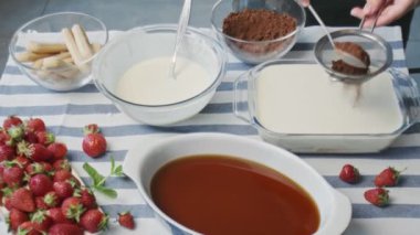 Profesyonel şef tiramisu keki pişiriyor. Genç ve çekici ev hanımı kakao tozuyla tiramisu kekinin tozunu alıyor.
