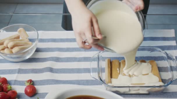 Chef profissional está cozinhando bolo tiramisu. Jovem dona de casa atraente derrama creme branco em tiramisu — Vídeo de Stock