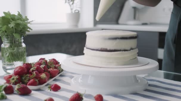 El chef profesional está cocinando pastel. Joven ama de casa atractiva pone crema blanca en el lado de la torta — Vídeos de Stock