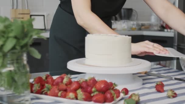 Професійний шеф-кухар готує торт. Молода приваблива домогосподарка використовує великий пластиковий шпатель і обертається стіл для вирівнювання білого крему на шоколадному торті — стокове відео
