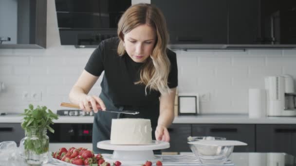 Professionell kock lagar tårta. Ung attraktiv hemmafru använder metall spatel justerar vit grädde på chokladkaka — Stockvideo