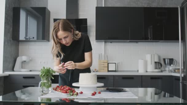 A profi séf tortát főz. Egy nő epret helyez egy gyönyörű fehér torta tetejére egy modern konyhában. — Stock videók