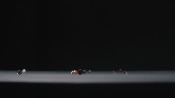 Χρωματιστές μεταλλικές καρφίτσες πέφτει σε μαύρο φόντο βίντεο αργής κίνησης. — Αρχείο Βίντεο