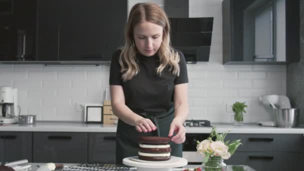 Profi-Koch kocht Kuchen. Junge attraktive Hausfrau macht süßen Schokoladenkuchen mit weißer Sahne und Erdbeere — Stockvideo