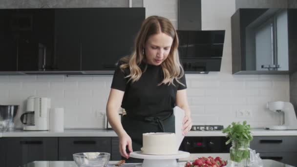 Professionell kock lagar tårta. Ung attraktiv hemmafru använder metall spatel justerar vit grädde på chokladkaka — Stockvideo