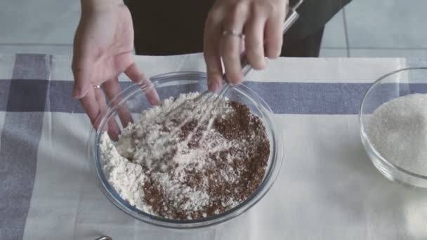 Chef profissional está cozinhando bolo. Jovem dona de casa atraente usa batedor de metal para misturar farinha e cacau na tigela — Vídeo de Stock